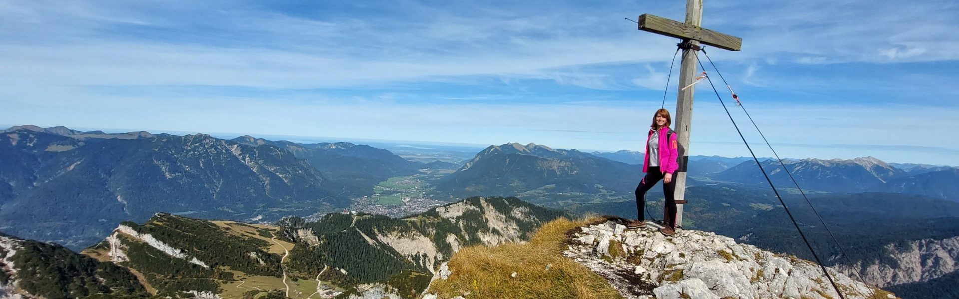 Christina Weichwald am Gipfelkreuz mit Blick über die Berge ins Tal
